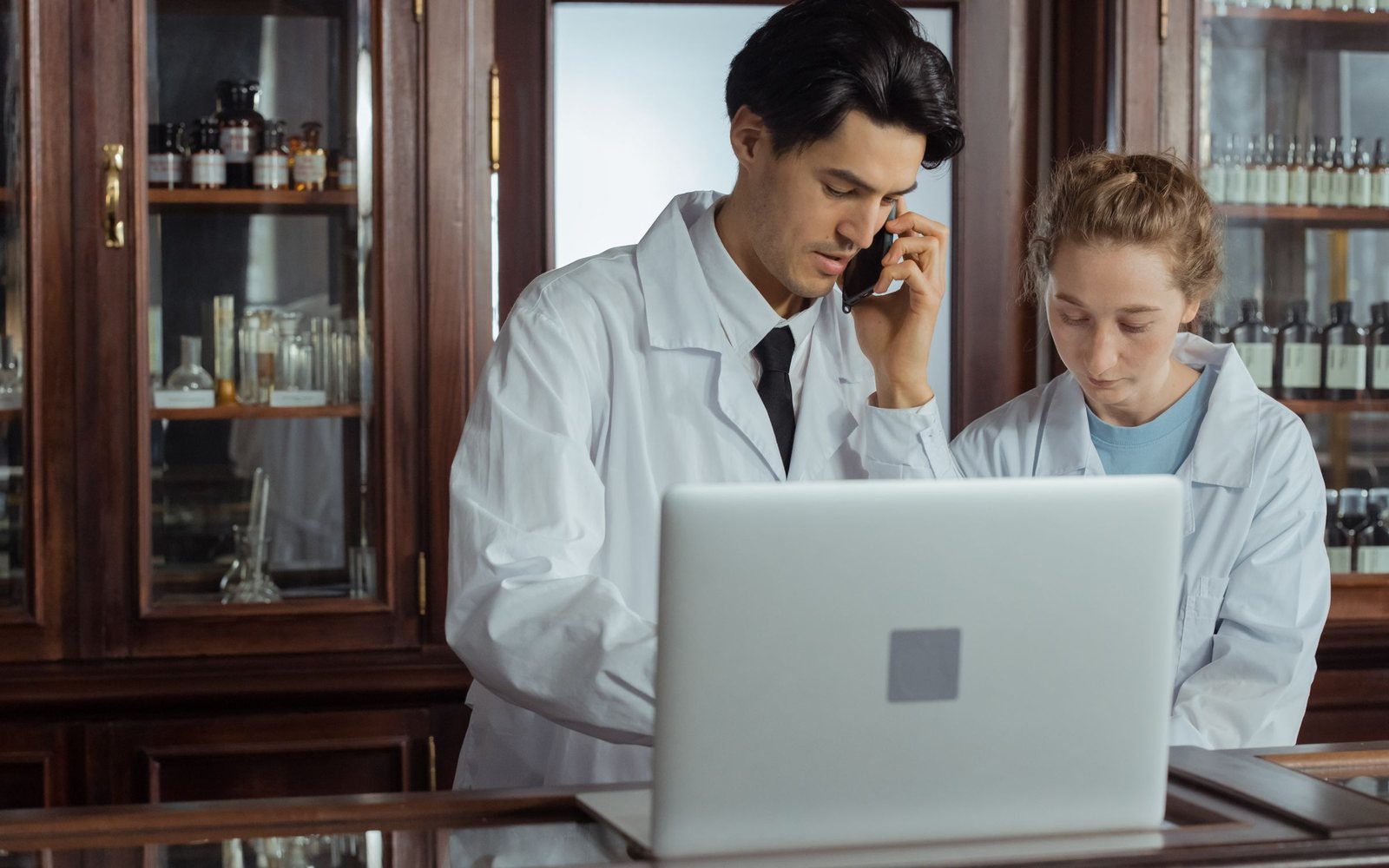 Pharmacists working with a laptop and phone behind a pharmacy counter